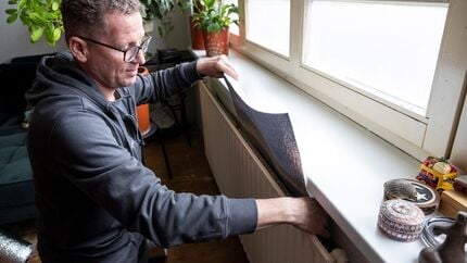 Radiatorfolie wordt aangebracht achter een radiator onder een vensterbank om warmteverlies te verminderen en energie te besparen. Op de vensterbank staan planten en decoratieve voorwerpen, waaronder tape en isolatiemateriaal.