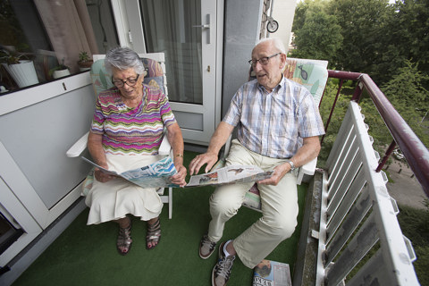 Twee ouderen zitten op het balkon een krant en tijdschrift te lezen.