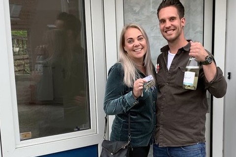 Vrouw en man houden sleutels en champagne omhoog en lachen. 