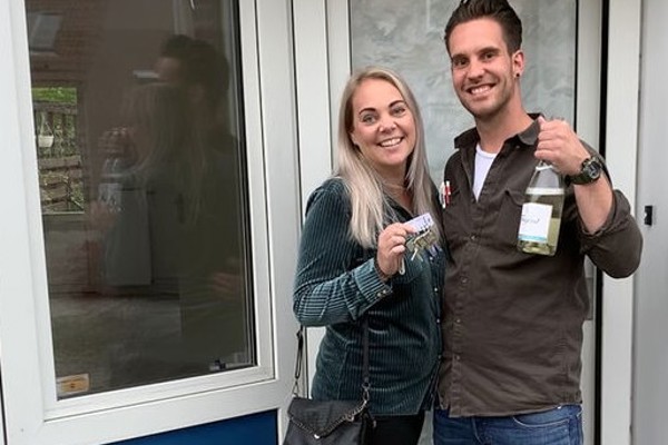 Vrouw en man houden sleutels en champagne omhoog en lachen. 