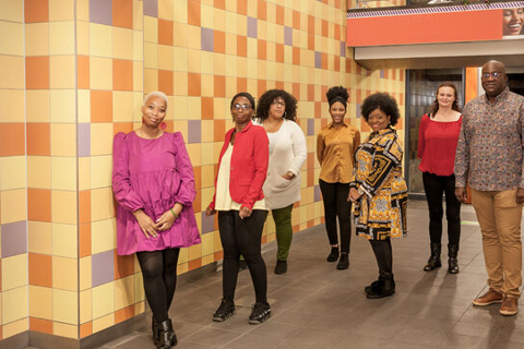 Zeven mensen lachen en staan op afstand van elkaar. 