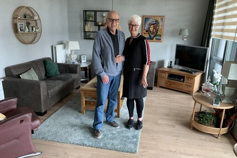 Twee ouderen lachen in woonkamer. 