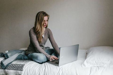 Meisje zit op bed achter laptop.