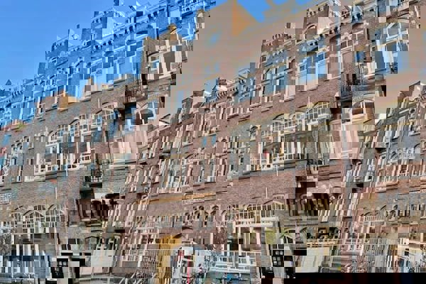 Historisch schoolgebouw van baksteen met sierlijke details en grote boogramen, fietsen geparkeerd voor de ingang.