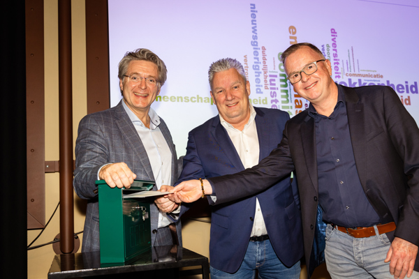 Foto van drie mannen poseren voor een post vak een heeft een envelop in zijn hand