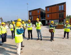 Een groep mensen met gele veiligheidsvesten en helmen staat op een bouwplaats