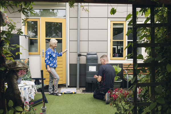 vrouw blauwe trui en man gebukt  bij een regenton