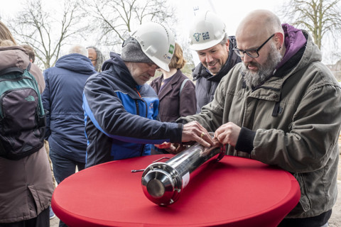 Drie mensen die een tijdcapsule dichtschroeven.