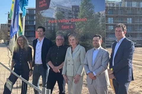 Een groep mensen staat op het terrein van het nieuwbouwproject Park Valley Diemen fase 4, met gebouwen die nog gebouwd worden op de achtergrond.